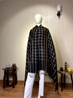 "Close-up detail of the soft black and gold wool shawl featuring a classic plaid checkered pattern and tassel fringe edges."