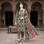 A mannequin seated on a traditional bench, wearing a black and gold paisley-patterned 3-piece unstitched lawn suit.