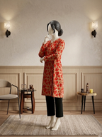 Mannequin wearing a red and beige floral print long shirt with a V-neckline and black trousers in a modern living room setting