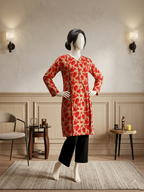 Mannequin wearing a red and beige floral print long shirt with a V-neckline and black trousers in a modern living room setting