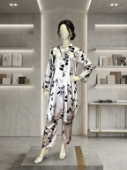A mannequin in a luxury boutique setting wearing a premium ivory silk-satin 2-piece suit with a black floral print. The mannequin is styled in a dynamic walking pose on a concrete platform with modern, minimalist backlit shelving in the background.