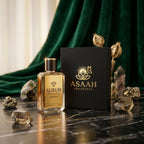 ASAAH Fragrance AURUM 50ml Eau De Parfum bottle next to its luxury matte black box with gold logo against a rich green velvet curtain.