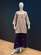 A mannequin wearing a light beige three-quarter sleeve tunic top and dark purple wide-leg pants with small floral motifs, displayed on a wooden floor against a dark blue background.