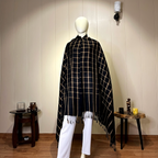 "Close-up detail of the soft black and gold wool shawl featuring a classic plaid checkered pattern and tassel fringe edges."