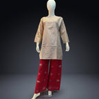 A mannequin wearing a loose beige tunic top with three-quarter sleeves and red wide-leg pants decorated with small gold floral motifs, set against a dark gray studio background.