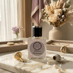 Front view of Maison Elegance perfume bottle displayed on a white marble slab with a gold funnel, delicate pearls, jewelry trays, and soft floral arrangements.