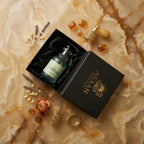 Top-down view of ASAAH Miss Perfume bottle in a luxury black satin-lined gift box with gold logo, jasmine flowers, and amber stones.