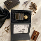 Top-down view of Oud De Saira perfume by ASAAH Fragrance sitting inside a premium satin-lined box next to raw oud wood chips and a leather notebook.