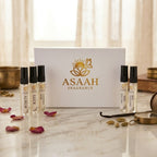 Five ASAAH Fragrance sample perfume vials including Aurum, Luck, Gorgeous Glow, Nera Pantera, and Miss Perfume standing upright on marble in front of a white and gold luxury box.