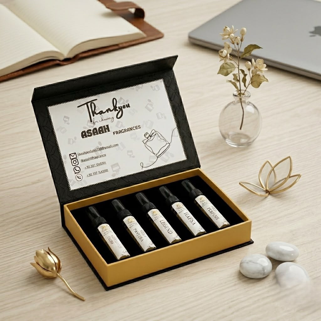 Open ASAAH Fragrance gold and black tester box on a wooden desk displaying five sample spray vials including Legend and Hafsa next to white jasmine flowers.