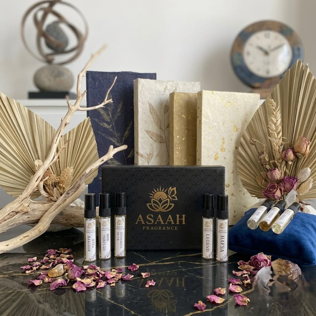 Open ASAAH Fragrance gold and black tester box on a wooden desk displaying five sample spray vials including Legend and Hafsa next to white jasmine flowers.