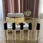 Five small perfume bottles on a wooden surface with a decorative clock and box in the background.