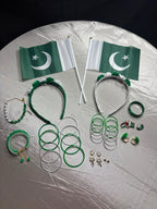 A collection of Pakistani-themed jewelry and accessories arranged on a silver tablecloth, including two small Pakistani flags, two green headbands with white flowers, several green and silver bangles, earrings, rings, and a beaded bracelet.